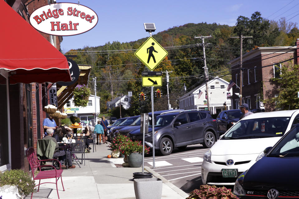 People walk past cafe table as cars park curbside, Wednesday Oct. 5, 2022, in Richmond, Vt. A town employee in Richmond is under fire for lowering the fluoride level in the drinking water below the state's recommended level for more than three years. A town commission has voted to return the water to full fluoridation after outrage from some residents. (AP Photo/Wilson Ring)