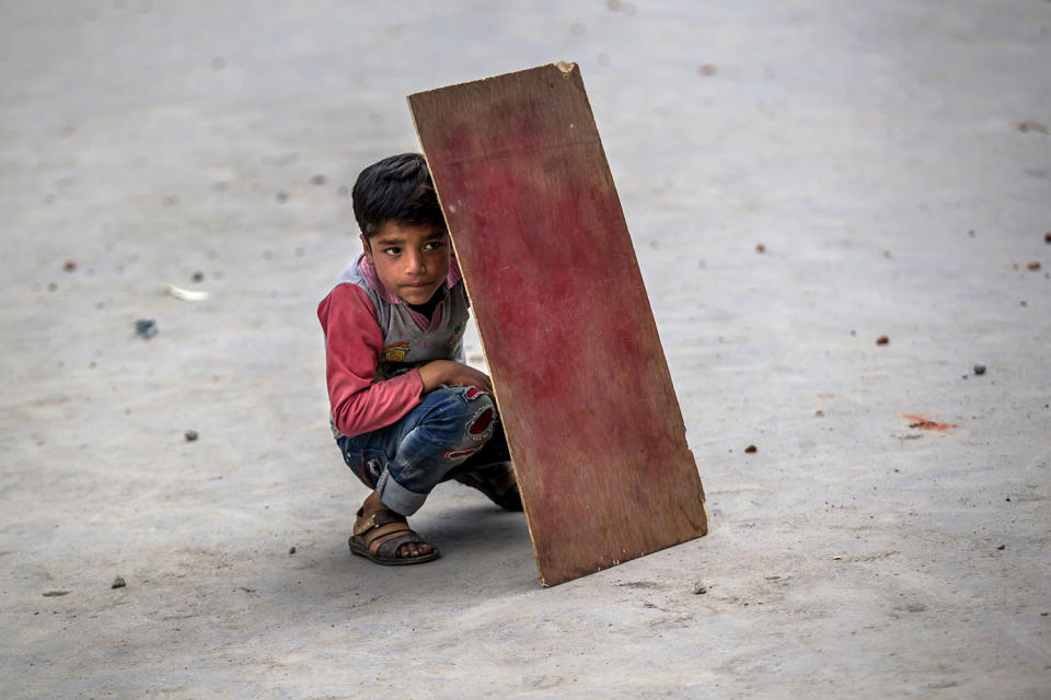 Kashmiri boy shields himself with plywood from stones during clashes