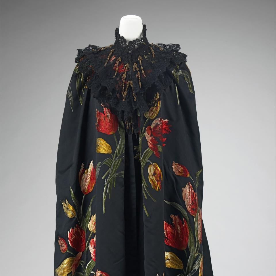 Elegant black cloak with bold floral pattern and intricate lace collar displayed on a mannequin