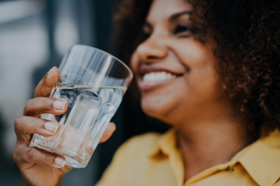 A person is smiling while holding a glass of water close to his face