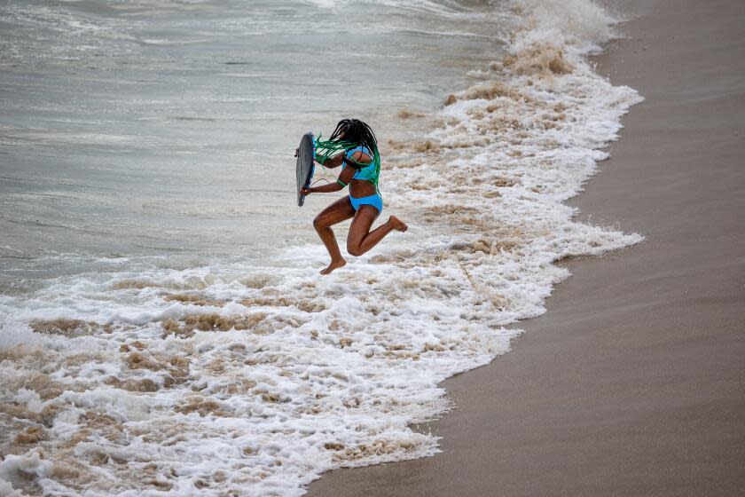 Newport Beach, CA - June 07: A beach goer leaps over a breaking wave while heading out to body board waves at Balboa Pier in Newport Beach Friday, June 7, 2024. (Allen J. Schaben / Los Angeles Times)