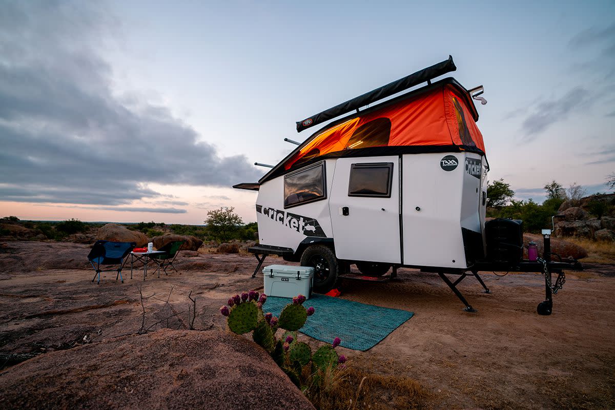 A white Taxa Outdoors Cricket with orange rooftop tent pictured against a desert landscape.