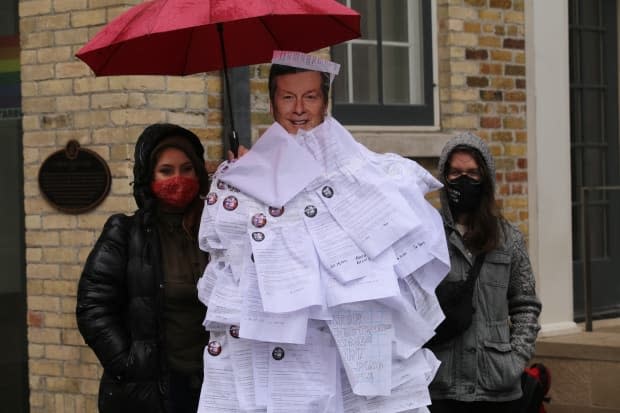 Protester outside the home of Toronto Mayor John Tory hold onto a cutout of the mayor that is covered with paper notices. The notices urge the mayor to drop an application for a court injunction against Toronto carpenter Khaleel Seivwright.  (Michael Charles Cole/CBC - image credit)