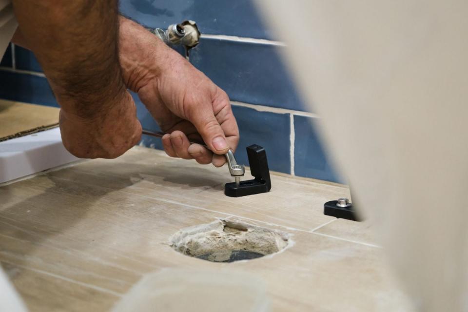 Hands makes repairs to a bathroom feature.