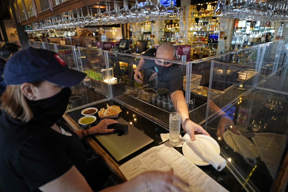 Bartender Daniel Vazquez, right, paces a plate to Betsy Campbell as she eats lunch at Picos Mexican restaurant Wednesday, March 10, 2021, in Houston. Picos, like many restaurants across the state, continue to operate at a reduced capacity and ask customers to wear masks despite Texas Gov. Greg Abbott ending state mandates for COVID-19 safety measures Wednesday. (AP Photo/David J. Phillip)