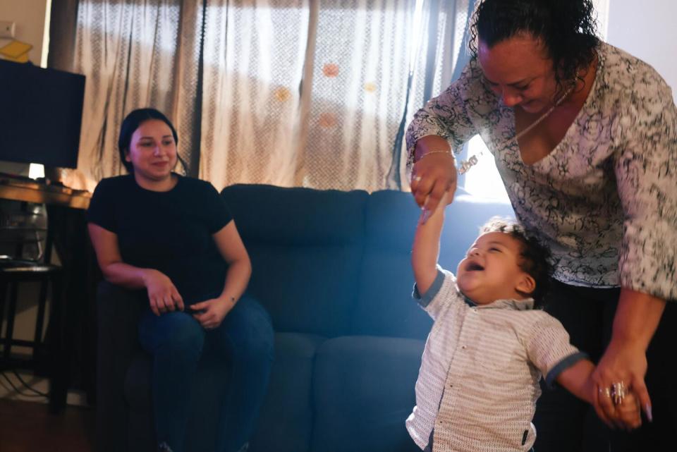 A toddler holds his grandmother's hands.