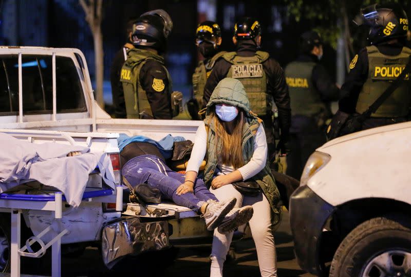 MATERIAL SENSIBLE. ESTA IMAGEN PUEDE OFENDER O MOLESTAR. Una mujer se sienta detrás de una camioneta junto a los cuerpos de personas que murireron después de que la policía allanó una discoteca clandestina para detener una fiesta prohibida, poco antes del inicio del toque de queda dominical debido a la pandemia de coronavirus, en Lima, Perú