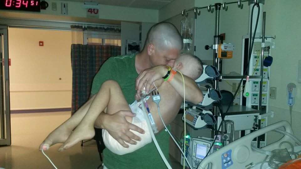 "I believe that this picture sums up what having a child with cancer is like. Our daughter was in the PICU for over four weeks. She had major complications right after her initial diagnosis of acute lymphocytic leukemia. She had about 14 or more surgeries back to back and she was in a weird state of unconscious consciousness. <br /><br /><strong>This was the first time her dad had the chance to hold her in more than two weeks.</strong> And it was very necessary as she had soiled everything on her bed, and the nurse was so tiny she couldn't change it all without help. So I (the mom) helped her. And Dad didn't want to put her back down. We were still unsure of her fate at the time I took this picture. Luckily, that was two years ago, and she's doing a lot better. Cancer in a child is one of the most evil things that can happen to a family, because it's unprovoked. It doesn't discriminate." -- Jen Johnston