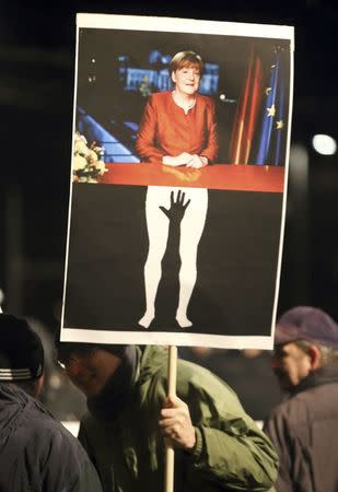 A members of LEGIDA, the Leipzig arm of the anti-Islam movement Patriotic Europeans Against the Islamisation of the West (PEGIDA), holds a placard showing German Chancellor Angela Merkel as he take part in a rally in Leipzig, Germany, January 11, 2016. REUTERS/Fabrizio Bensch