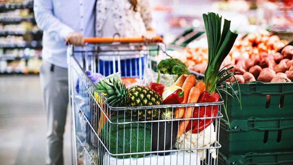 Unrecognizable young couple with a full shopping cart of groceries at a convenience store.