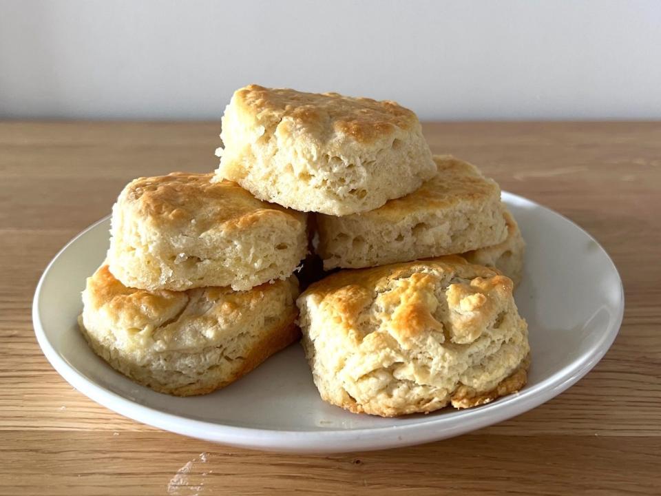 A pile of biscuits on a white plate on top of a wood surface.