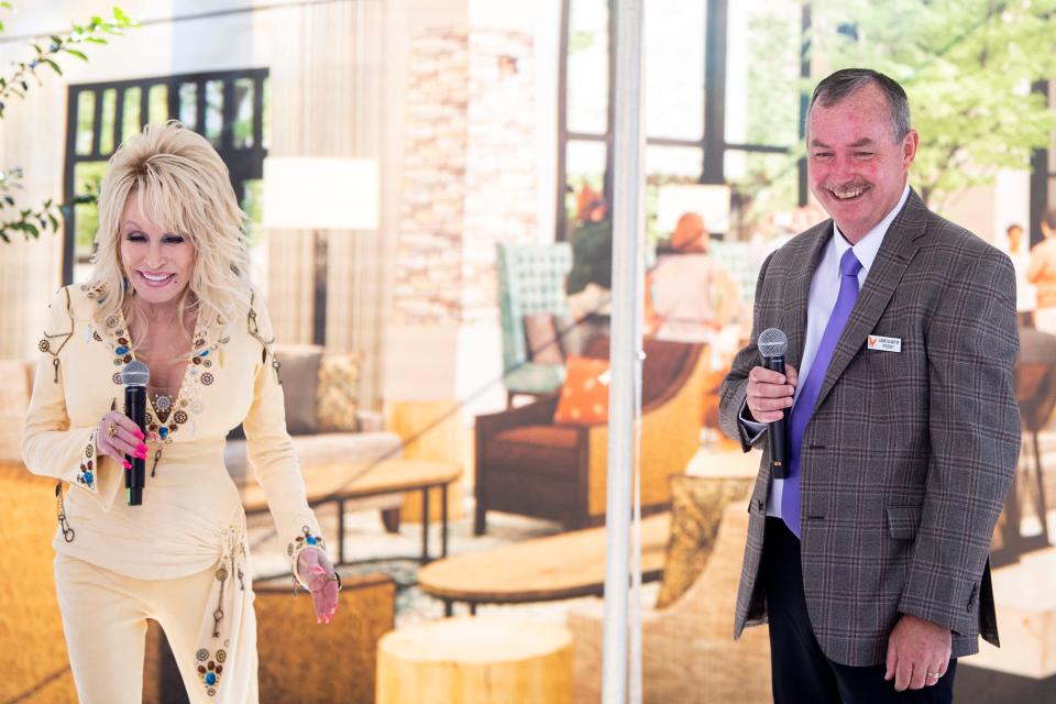 Dolly Parton and Dollywood Parks & Resorts President Eugene Naughton share an update on Dollywood's HeartSong Lodge & Resort in front of a rendering of its lobby during an event Friday. The resort is slated to open in fall 2023, but guests should be able to start making reservations during the first few months of 2023. It's part of a planned $500 million expansion over the next decade.