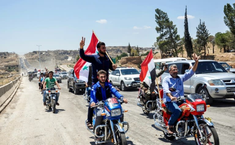 Motorcyclists carry Syrian national flags and wave as they drive along the M5 highway between Homs and Hama in the centre of the country