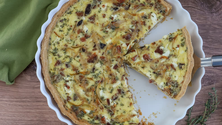 baked bacon, onion, and goat cheese quiche in a pan, sliced up
