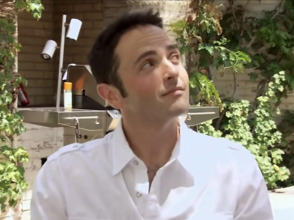 Jimmy Karz wearing a white shirt in a garden and looking up to his left