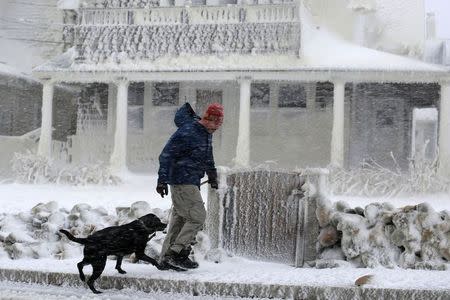 A man walks his dog past an ocean front house covered in ice during a winter blizzard in Marshfield, Massachusetts January 27, 2015. REUTERS/Brian Snyder