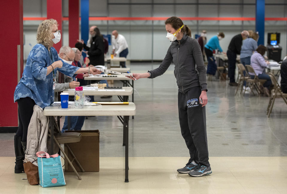 Bridget McDonald, right, receives a ballot from poll worker Patty Piek-Groth on Tuesday, April 7, 2020, at the Janesville Mall in Janesville, Wis. Hundreds of voters in Wisconsin are waiting in line to cast ballots at polling places for the state's presidential primary election, ignoring a stay-at-home order over the coronavirus threat. (Angela Major/The Janesville Gazette via AP)