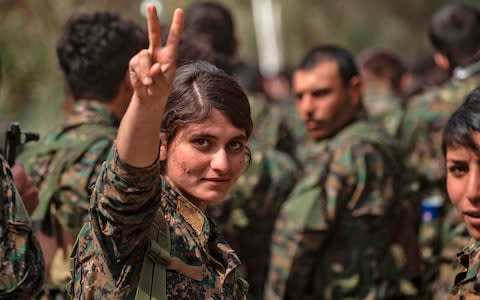 A female fighter of the US-backed Kurdish-led Syrian Democratic Forces (SDF) flashes the victory gesture while celebrating after announcing the total elimination of the Islamic State in Syria - Credit: AFP