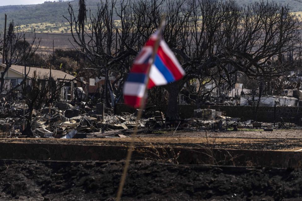 A Hawaiian flag stands near a residential area devastated by a wildfire in Lahaina, Hawaii, Saturday, Aug. 19, 2023. As days turn into weeks, the odds are growing longer for families hoping to be reunited with missing loved ones after the fire swept across Hawaii's town of Lahaina. (AP Photo/Jae C. Hong)