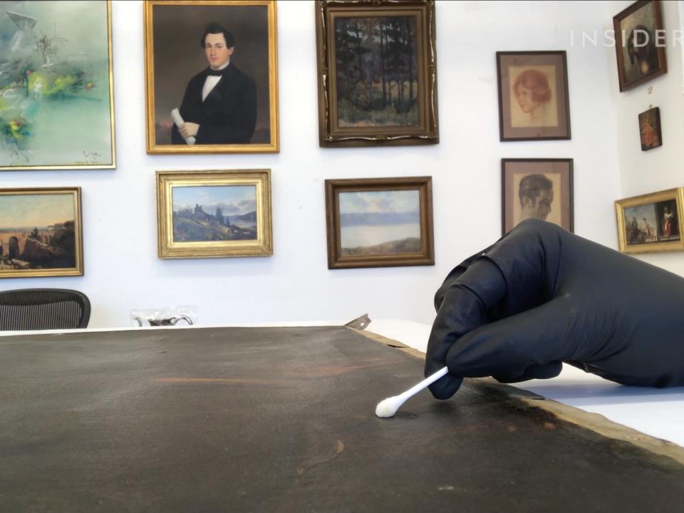 A Q-tip being used to remove residues from the surface of a painting.