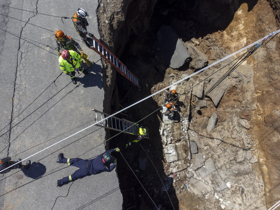 Rescuers descend into a sinkhole in Villa Nueva, Guatemala, Sunday, Sept. 25, 2022. Rescuers are searching for people who are believed to have fallen into the sinkhole while driving their vehicle, while four others were rescued alive from the scene on Saturday night. (AP Photo/Moises Castillo)