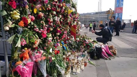 A man takes a picture of flowers on the fence by Ahlens department store following Friday's attack in central Stockholm, Sweden, April 9, 2017. REUTERS/Philip O'Connor