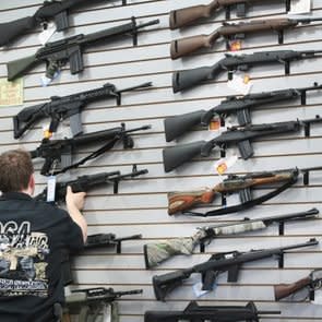 guns displayed on a wall in a store with an anonymous gun salesman