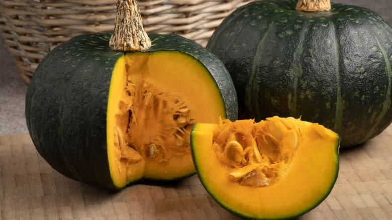 Quarters of kabocha and whole kabocha on wood cutting board