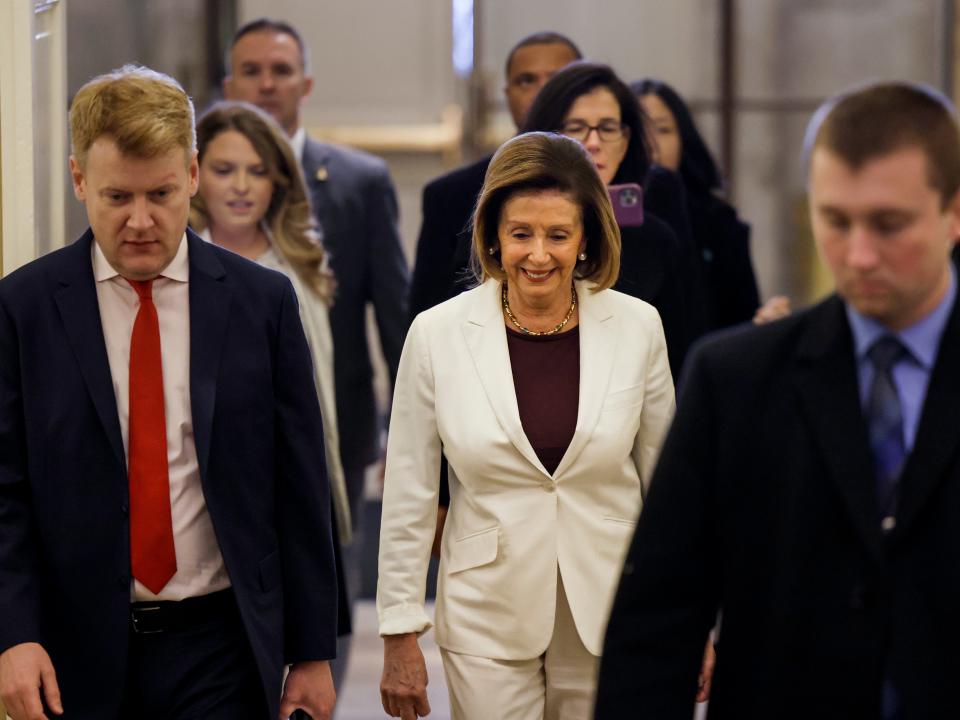 House Speaker Nancy Pelosi wears a white suit and brown shirt as she walks into Congress with her team.