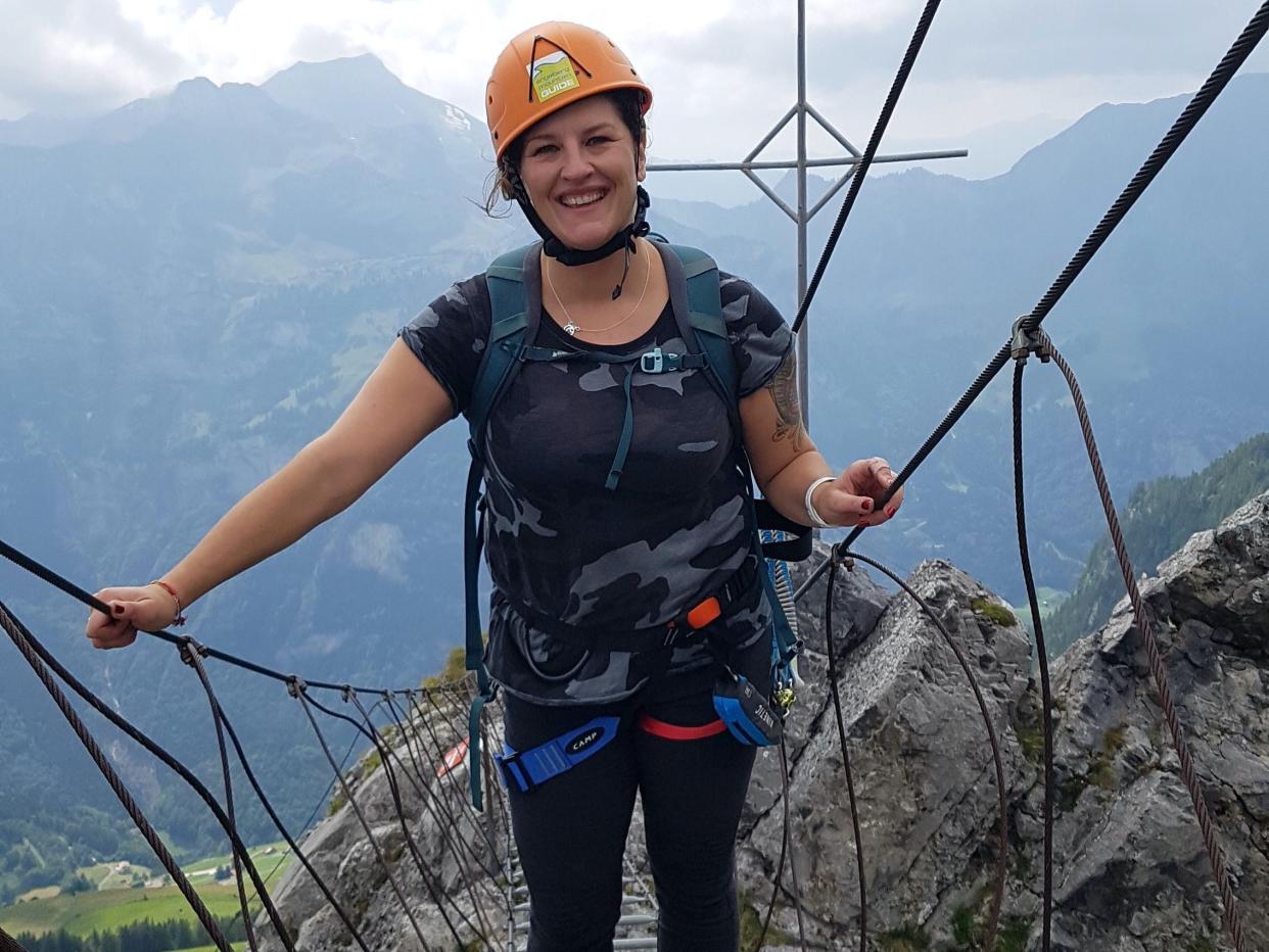 Woman wearing an orange helmet crossing suspension bridge in Switzerland.