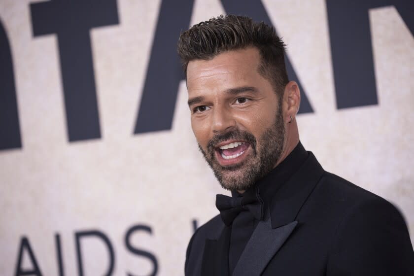 A man with short brown hair and a beard posing in a black suit