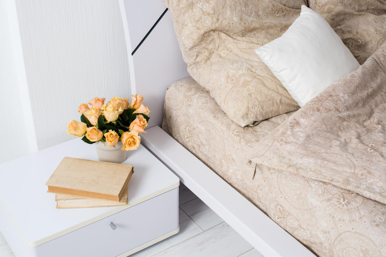 Bright white bedroom interior, cozy bed with beige linen, flowers on a bedside table, closeup