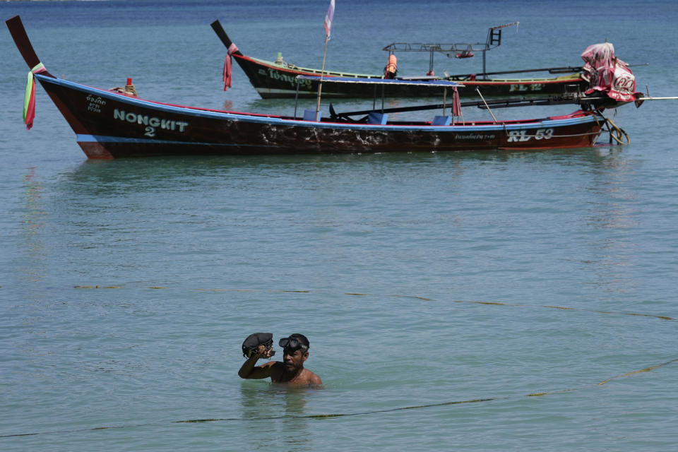 Tour boat owner Somsak Betlao wades in shore in the shallow waters of Patong Beach on Phuket province, southern Thailand, June 28, 2021. Somsak is putting his hope on a government scheme to bring the tourists back starting July 1 known as the "Phuket Sandbox." Even though coronavirus numbers are again rising around the rest of Thailand and prompting new lockdown measures, officials say there's too much at stake not to forge ahead with the plan to reopen the island to fully-vaccinated travelers. (AP Photo/Sakchai Lalit)