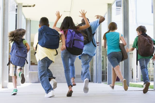 Rear view of elementary school pupils running outside