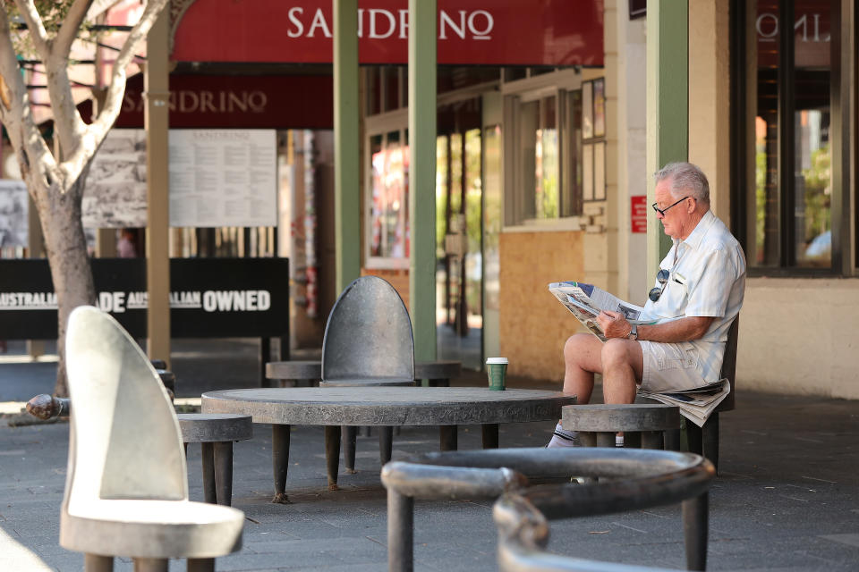 A man reads a local newspaper while sitting on roadside seating on South Terrace on March 26, 2020 as local newspaper cut in major News Corp cull