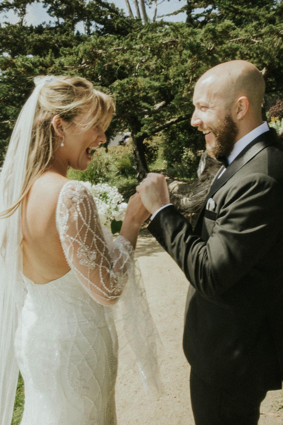 A bride and groom hold hands and smile at each other.