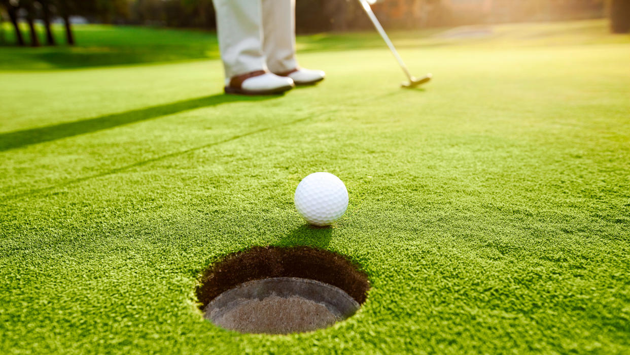 An early morning sun lights up the golf ball as it travels into the hole in the well-manicured grass.