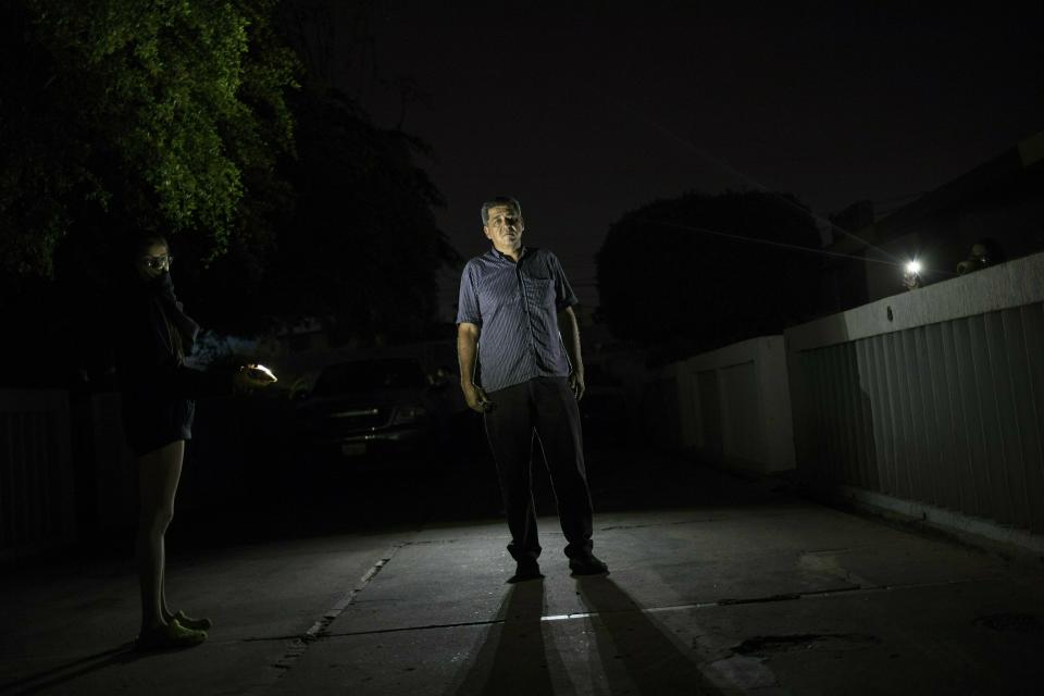 In this May 23, 2019 photo, Wilfido Briñez poses for photo while being illuminated by her daughter's cell phone, during a black out in Maracaibo, Venezuela. As Venezuela's crisis deepens, the sale of electric generators is one of the few growth industries in the once-wealthy oil nation, whose residents struggle to get through each day as public services crumble. (AP Photo/Rodrigo Abd)