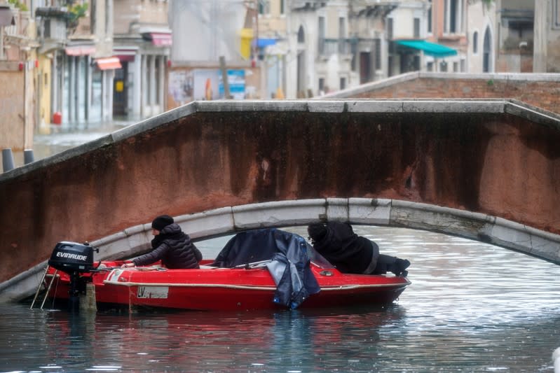A boat tries to pass under a bridge during a period of seasonal high water in Venice