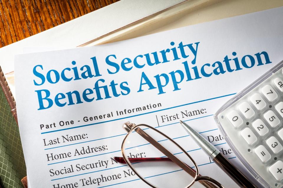 A pair of glasses, a pen and a calculator placed on a social security benefits application form.