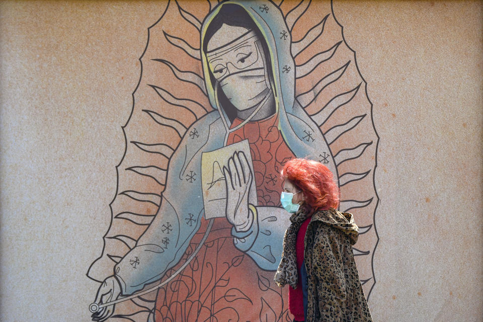 A woman walks by a depiction of a medical staff wearing protective equipment inspired by the famous Our Lady of Guadalupe Catholic icon in Bucharest, Romania, Wednesday, April 29, 2020. The artwork, among others depicting medical staff in the manner of religious icons, created by designer Wanda Hutira, is part of a campaign called Thank You Doctors, meant to raise awareness to the work of medical staff fighting the COVID-19 pandemic. Following public pressure by Romania's influential Orthodox church the artworks, described as "blasphemous" will be removed from all locations in the Romanian capital, according to the agency behind the project. (AP Photo/Andreea Alexandru)