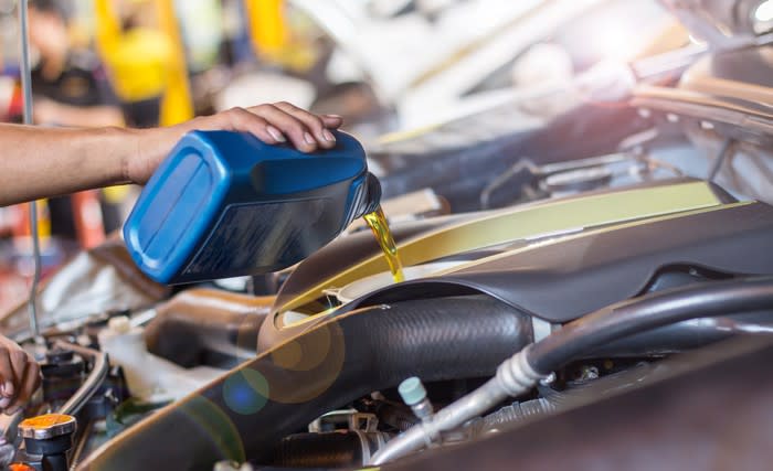 Man pouring oil into vehicle engine.