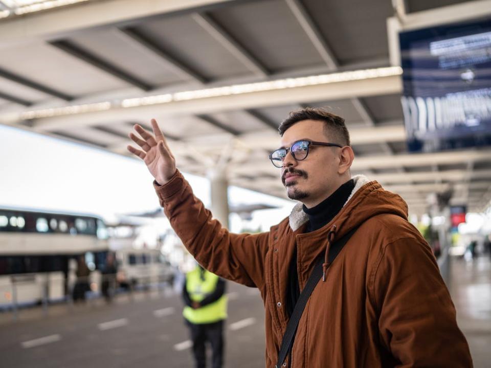 Man hailing a cab outside an airport.