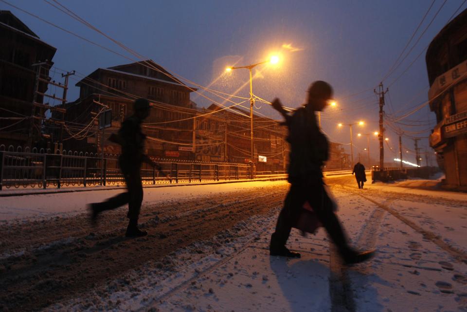 Indian policemen cross a road during snowfall on a cold winter morning in Srinagar December 31, 2013. Temperatures in Srinagar, which received the season's second snowfall on Tuesday, dipped to -1.4 degrees Celsius (29.5 degrees Fahrenheit), according to India's metrological department website. REUTERS/Danish Ismail (INDIAN-ADMINISTERED KASHMIR - Tags: ENVIRONMENT)