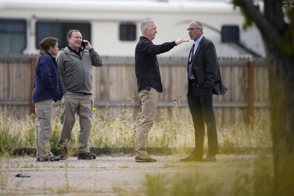 Fremont County, Colo., coroner Randy Keller, far right, meets with fellow authorities outside a closed funeral home where 115 bodies have been stored, Friday, Oct. 6, 2023, in Penrose, Colo. Authorities are investigating the improper storage of human remains at the southern Colorado funeral home that performs "green" burials without embalming chemicals or metal caskets. (AP Photo/David Zalubowski)