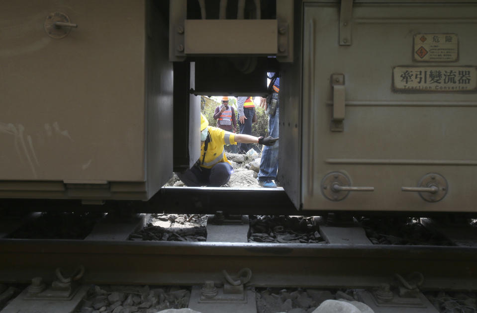 Workers examine the derailed train near Taroko Gorge in Hualien, Taiwan on Saturday, April 3, 2021. The train partially derailed in eastern Taiwan on Friday after colliding with an unmanned vehicle that had rolled down a hill, killing and injuring dozens. Workers began removing some of the train cars and repair work also has begun on the tracks including the tunnel where part of the eight-car train crashed. (AP Photo/Chiang Ying-ying)