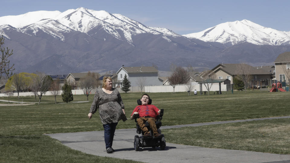 FILE - In this on April 14, 2020, file photo, Jodi Hansen walks with her son Jacob Hansen near their home in Eagle Mountain, Utah. Utah overhauled crisis guidelines Thursday, Aug. 20, 2020, that could have put people with disabilities at the back of the line if hospitals become overwhelmed during the coronavirus pandemic, adopting a new plan that federal officials said should serve as a national model for removing bias from life-or-death decisions. In Utah, the complaint was filed on behalf of Hansen, who has cystic fibrosis that affects his lungs and uses a wheelchair due to cerebral palsy. (AP Photo/Rick Bowmer, File)