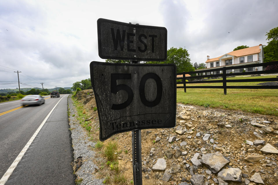 Motorists pass a highway sign covered in black substance situated in front of a historic mansion turned event space, right, near a Jack Daniels barrelhouse complex, Wednesday, June 14, 2023, in Mulberry, Tenn. A destructive and unsightly black fungus which feeds on ethanol emitted by whiskey barrels has been found growing on property near the barrelhouses. (AP Photo/John Amis)