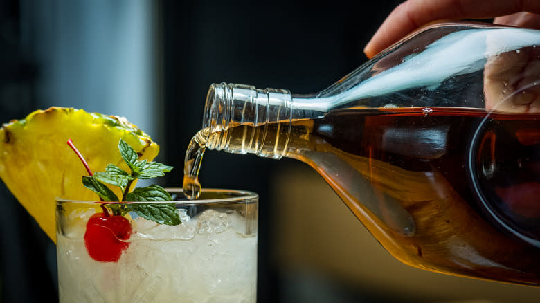 Rum being poured from a bottle into a garnished cocktail