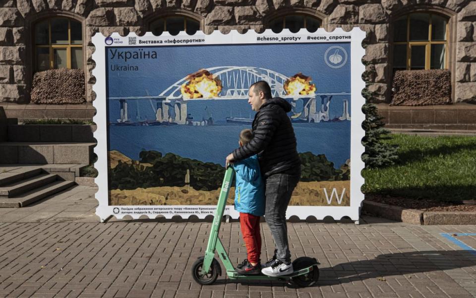 <div class="inline-image__title">1243909846</div> <div class="inline-image__caption"><p>A man rides a scooter with a child in front of an image of a stamp showing explosions on the Kerch Bridge, a key supply route Russia built after it illegally annexed Crimea, on Oct. 12, 2022 in Kyiv, Ukraine. </p></div> <div class="inline-image__credit">Metin Aktas/Anadolu Agency via Getty Images</div>